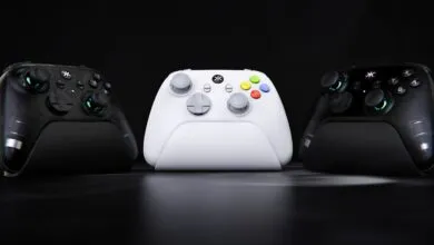 Three gaming controllers, two black and one white, arranged on a dark surface.