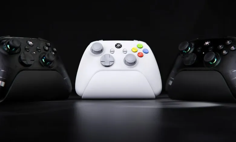Three gaming controllers, two black and one white, arranged on a dark surface.