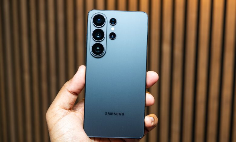 Hand holding a gray Samsung Galaxy phone showing the camera lenses.