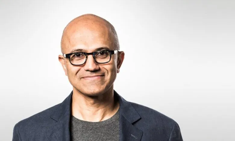 Satya Nadella, Microsoft CEO, smiles wearing glasses and a blazer.
