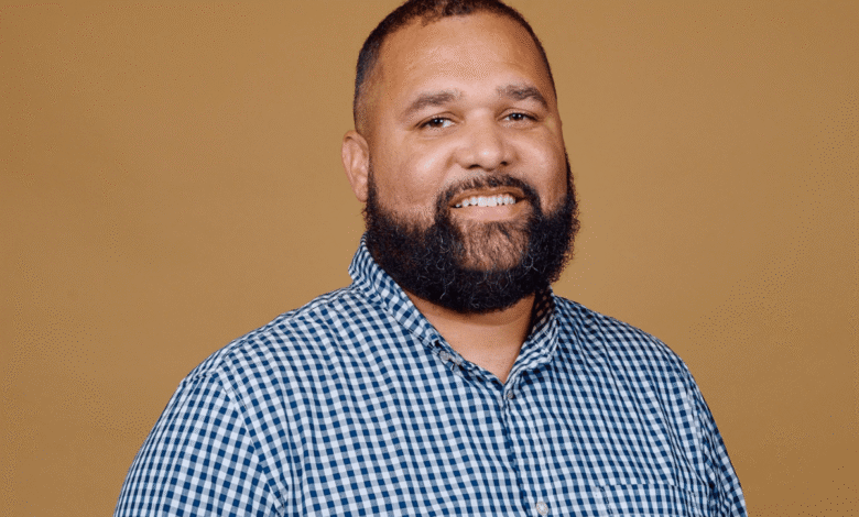 Portrait of a smiling man with a beard wearing a blue and white checkered shirt.