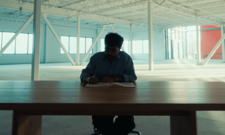 Man writing in notebook at large table in empty warehouse.