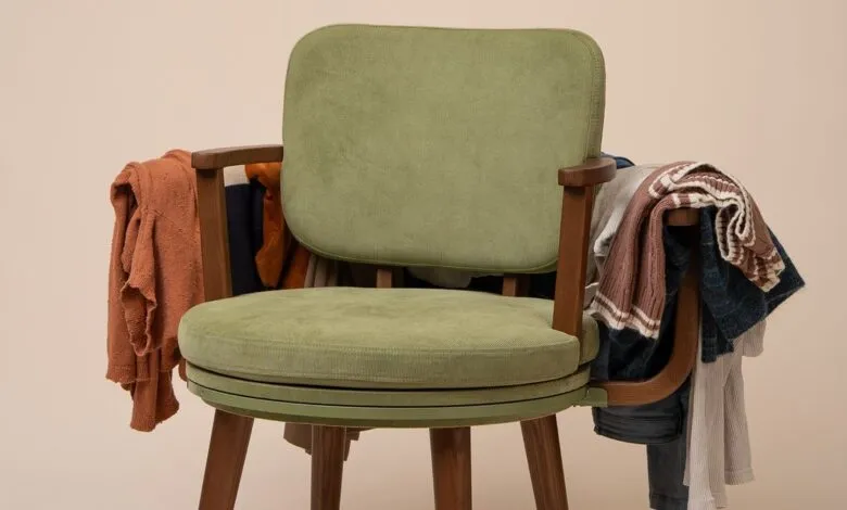 Green chair draped with colorful clothing, creating a cozy, cluttered feel.