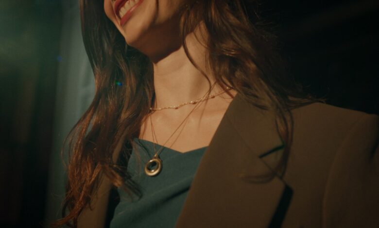 Smiling woman with brown hair wearing a blazer and layered necklaces.