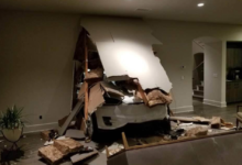 White car crashed through living room wall, causing significant damage.
