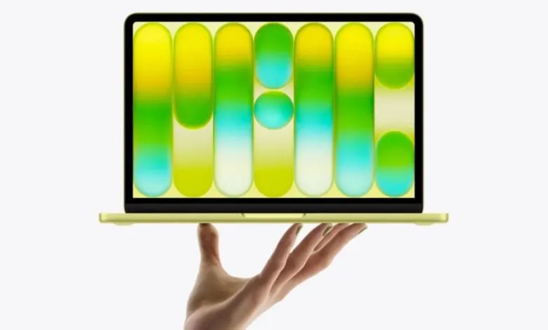 Hand holding a yellow MacBook Air with a colorful, abstract wallpaper.