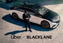 Man in suit stands next to a black and white luxury car on a brick driveway.