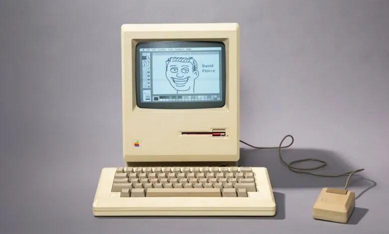 Vintage Macintosh computer with a drawing of a face on the screen.