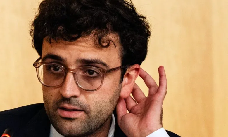 Man with glasses holds hand to ear, listening intently.