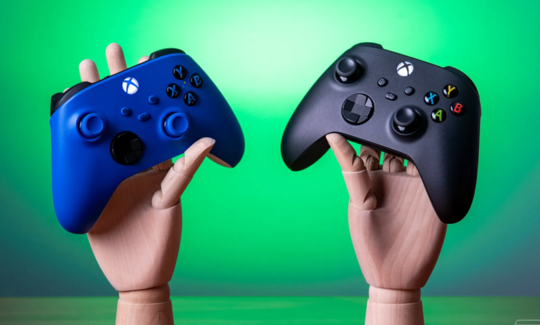 Two wooden hands hold blue and black Xbox Wireless Controllers against green backdrop.