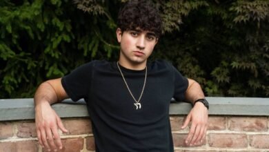 Portrait of a young man with curly hair leaning against a brick wall.