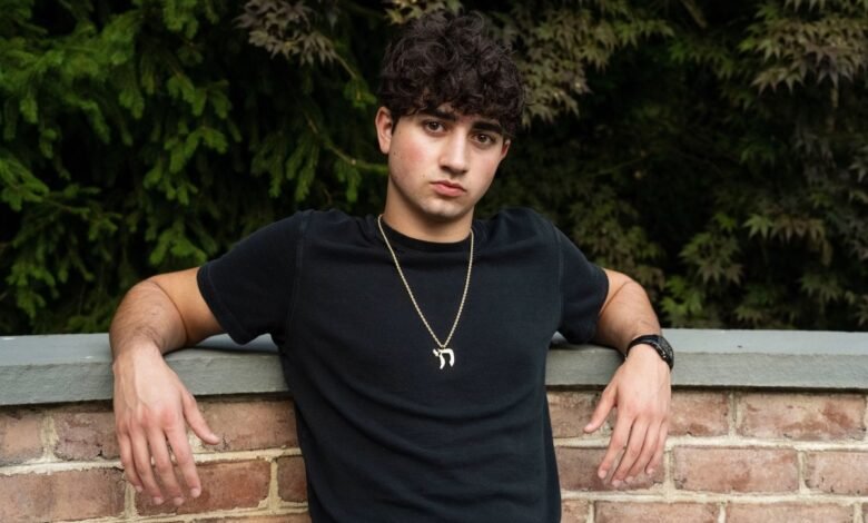 Portrait of a young man with curly hair leaning against a brick wall.
