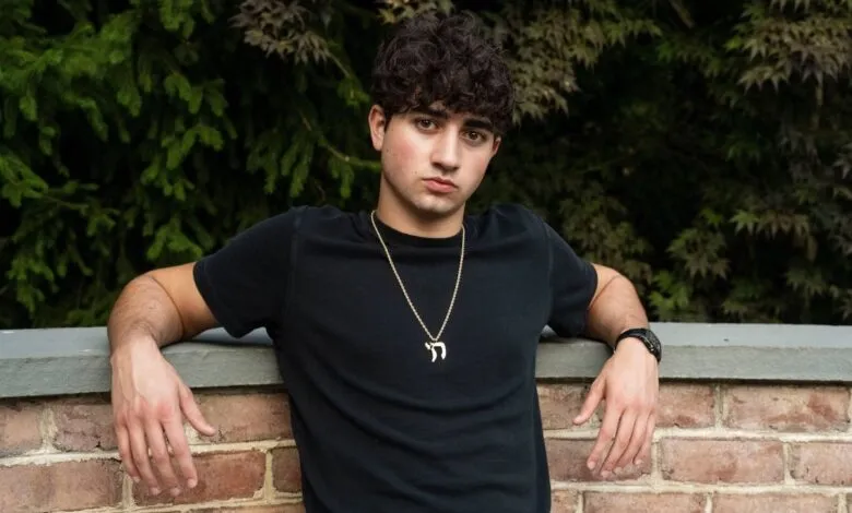 Portrait of a young man with curly hair leaning against a brick wall.