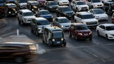 Zoox robotaxi navigates city streets amidst other vehicles.
