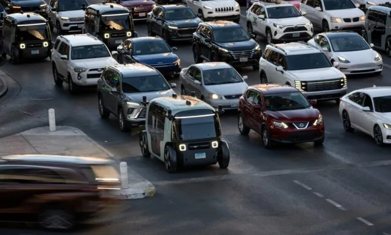 Zoox robotaxi navigates city streets amidst other vehicles.