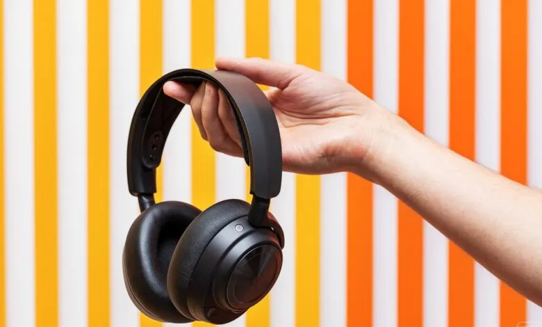 Hand holding black over-ear headphones against striped background.