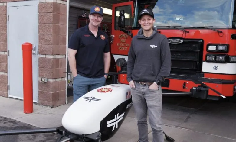 Two men stand with a drone in front of an Aspen fire truck.