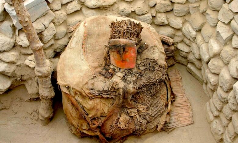 Ancient burial bundle with a red mask, surrounded by stone walls and sand.