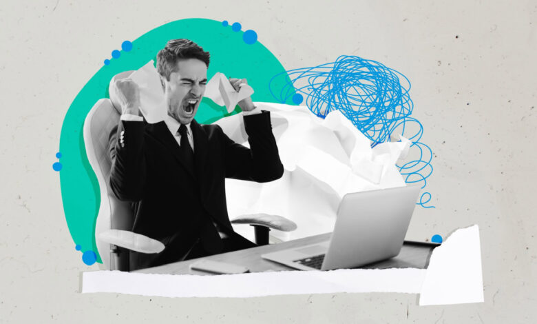 Frustrated man in suit tears paper at desk with laptop.