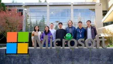 Group of eight people stand behind the Microsoft sign outside a building.
