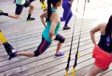 Group fitness class using TRX suspension training on wooden deck.