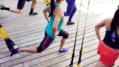 Group fitness class using TRX suspension training on wooden deck.