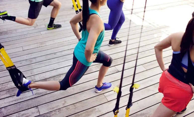 Group fitness class using TRX suspension training on wooden deck.