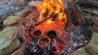 Three clay pots cooking in a campfire surrounded by rocks and wood.