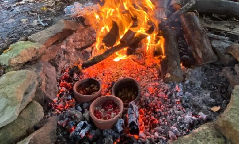 Three clay pots cooking in a campfire surrounded by rocks and wood.