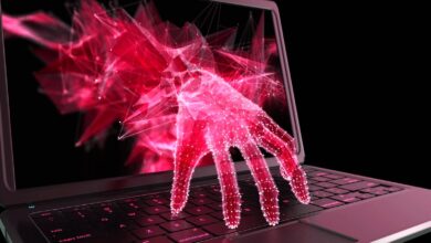 Abstract red hand emerging from laptop screen, touching keyboard.