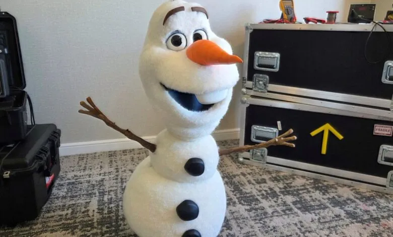 Olaf from Frozen stands next to equipment cases in a room.