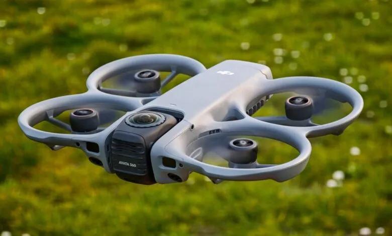 Gray DJI Avata drone hovering over green grass, propellers visible.