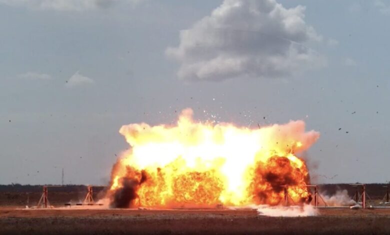 Large explosion with orange flames and debris against a cloudy sky.