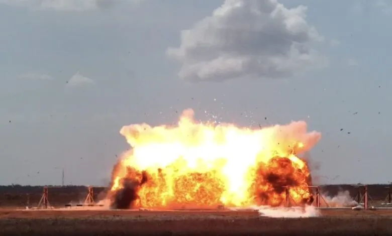Large explosion with orange flames and debris against a cloudy sky.