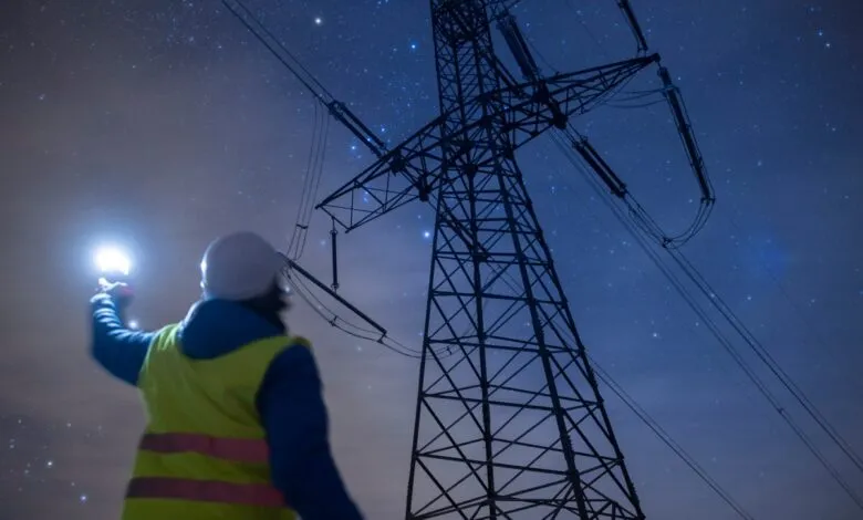 Electrical worker inspects power lines at night with flashlight.