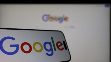 Smartphone displays Google logo in front of a blurred Google webpage on a monitor.