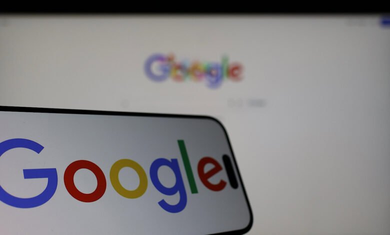 Smartphone displays Google logo in front of a blurred Google webpage on a monitor.