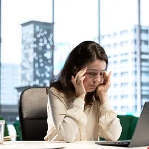 Woman at desk with hands on temples, appearing stressed or in pain.