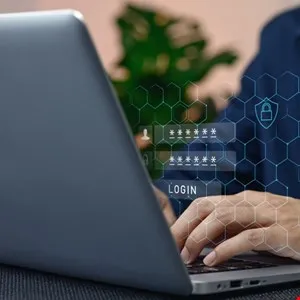 Person typing on laptop with login screen overlay showing username, password, and security icon.