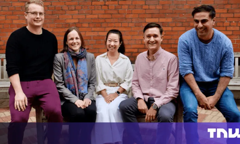 Five smiling people sit on a bench in front of a brick wall.