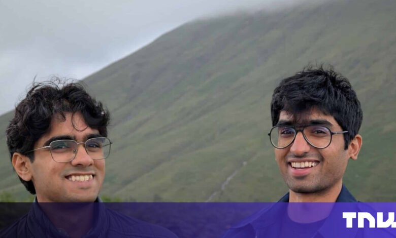 Two smiling young men pose in front of a green, misty mountain.