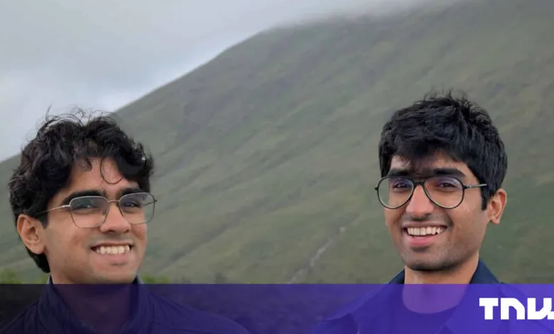 Two smiling young men pose in front of a green, misty mountain.