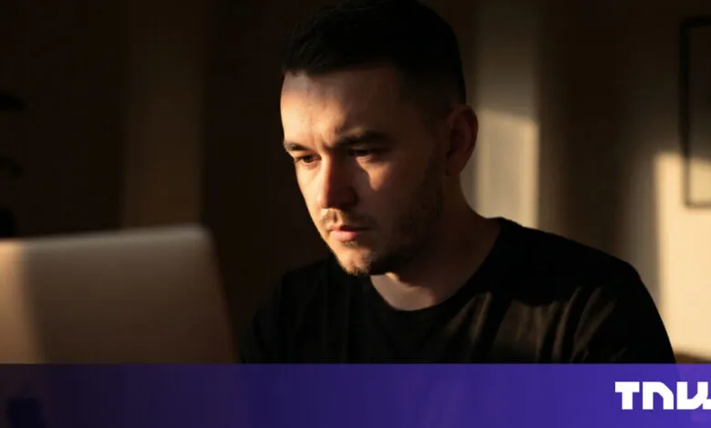 Man focused on laptop screen in warm, shadowed room.