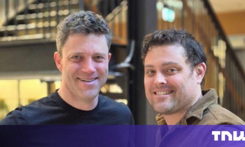 Two smiling men pose indoors with a modern staircase visible behind them.