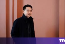 Portrait of a man in a black coat against a pink wall.