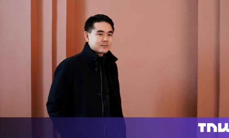 Portrait of a man in a black coat against a pink wall.