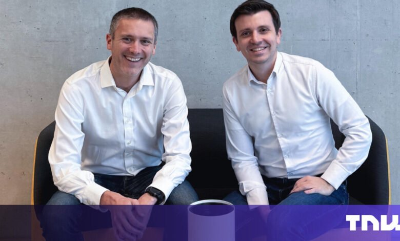 Two smiling men in white shirts sit side-by-side on a modern chair.