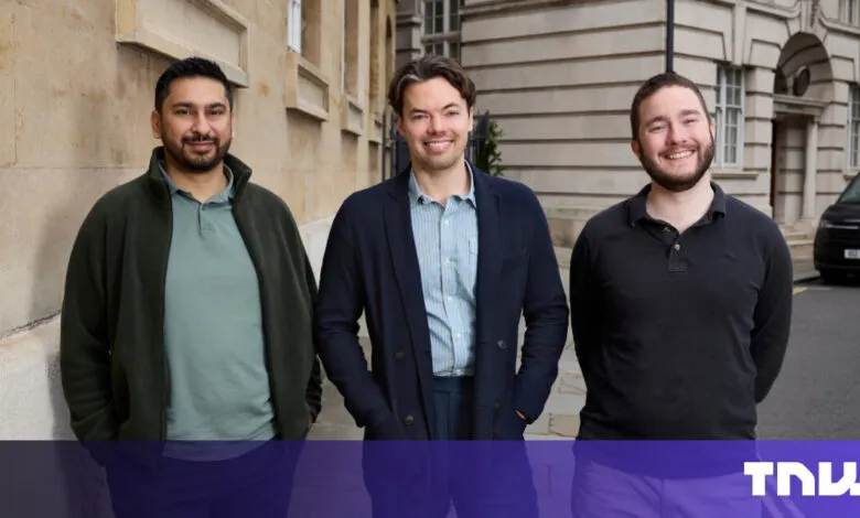 Three smiling men stand outdoors in front of a building and a parked van.