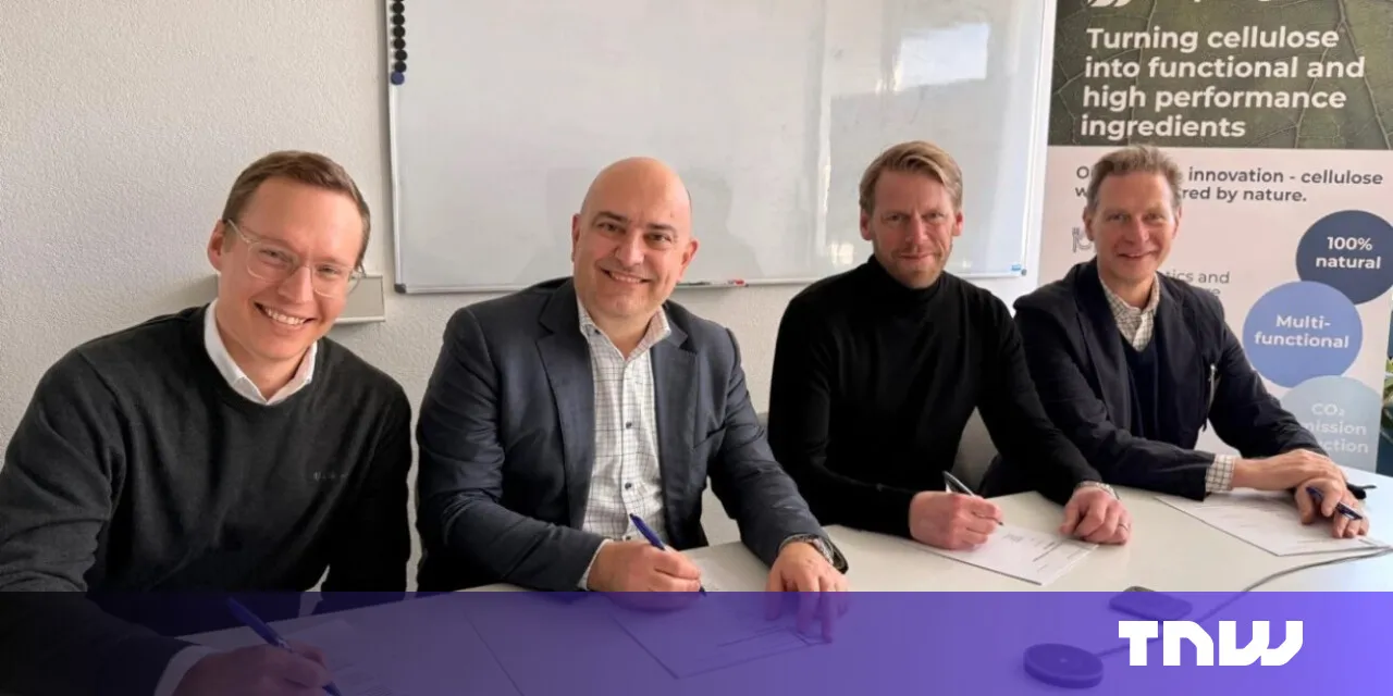 Four smiling business professionals sign an agreement at a table.