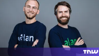 Two men smiling, wearing branded sweaters against a gray background.